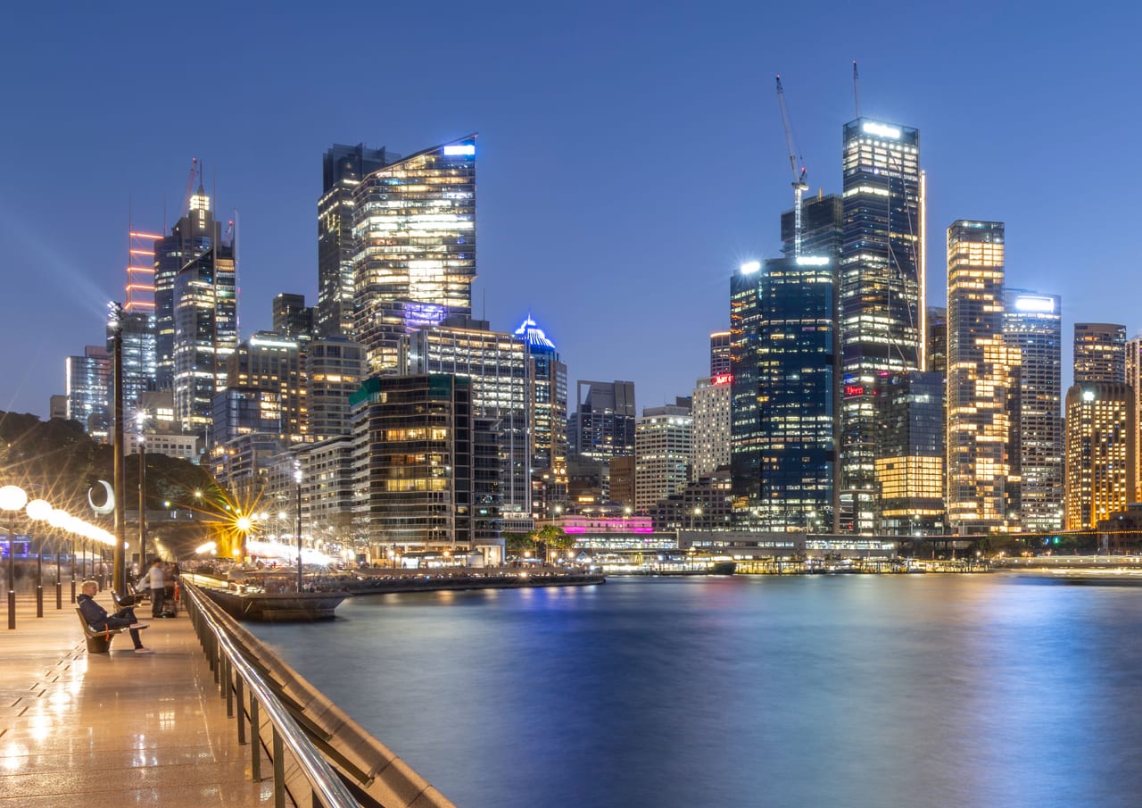 Illuminated Sydney waterfront buildings and reflections at blue hour.