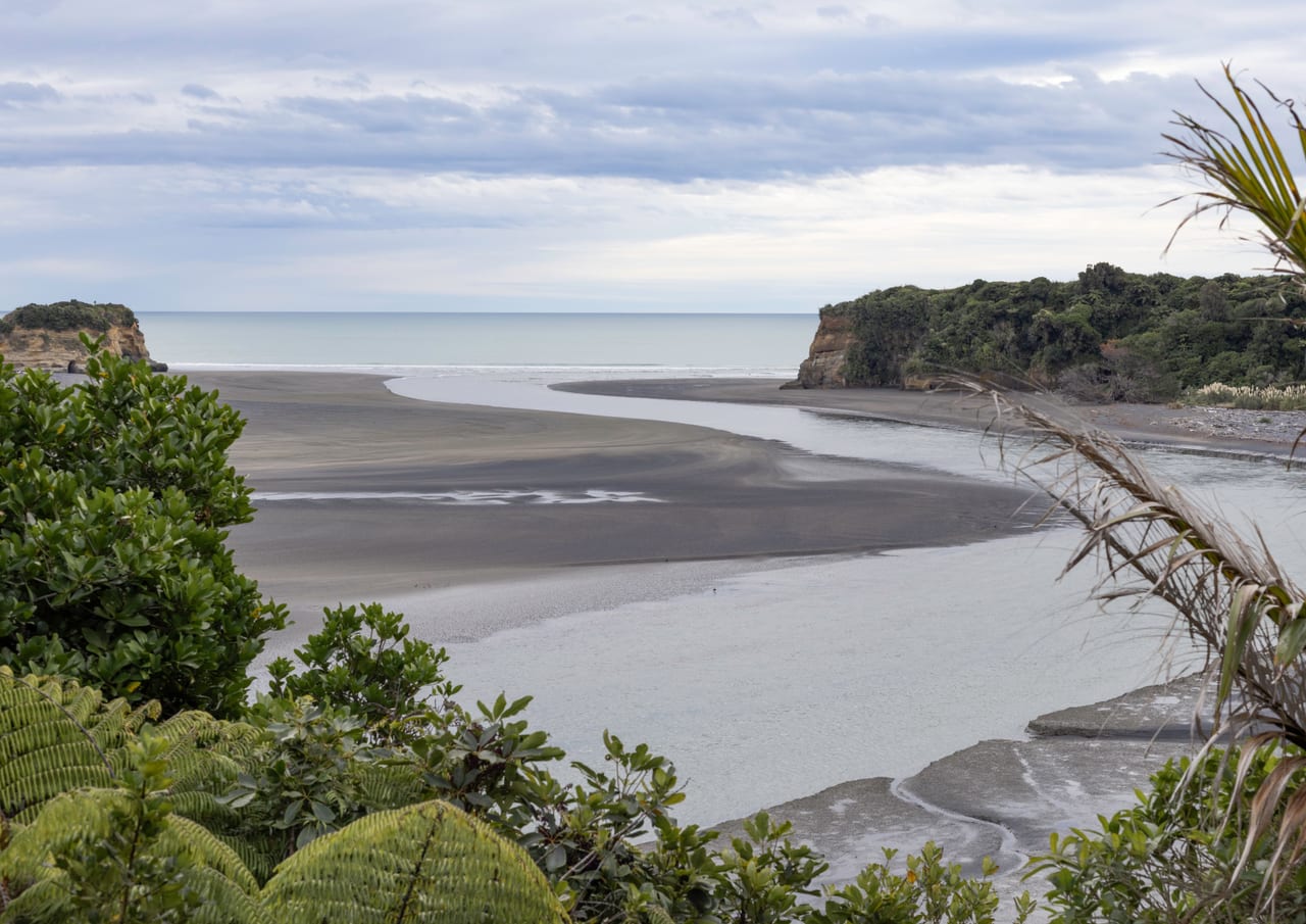 A serene river mouth meeting the sea, surrounded by greenery and cliffs.