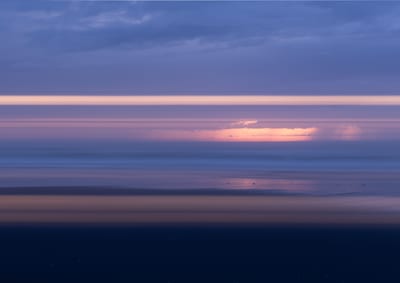 Soft pink sunset light above blue coastal water.