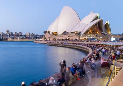 Sydney Opera House beside blue harbour water and a waterfront walkway.